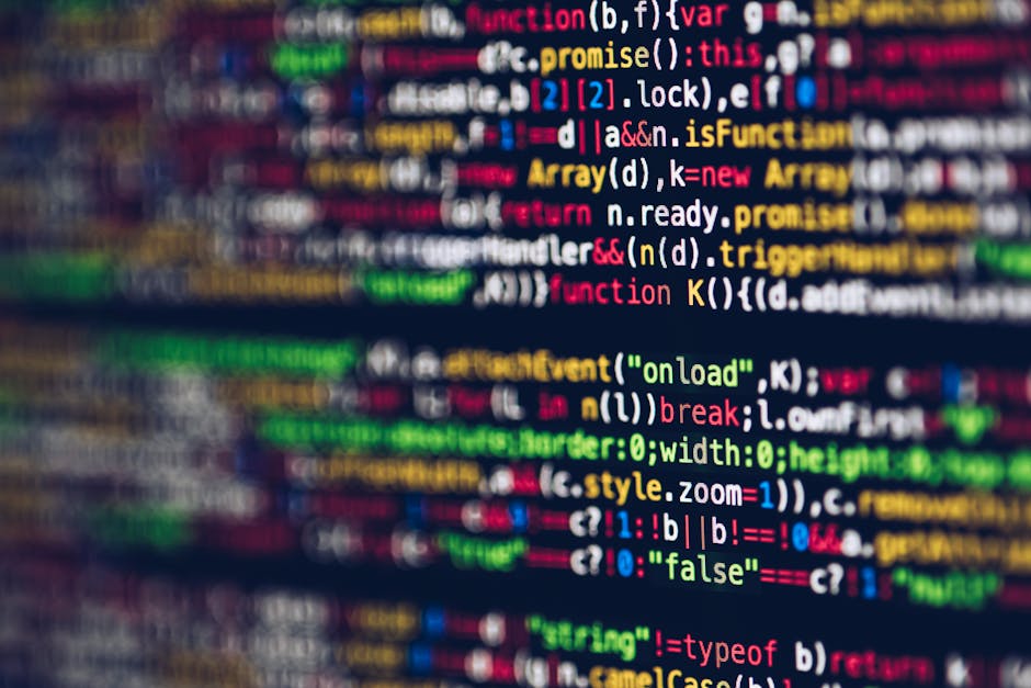 A close-up view of a laptop computer displaying lines of programming code on its screen, which is slightly tilted and showing syntax highlighting with various colors on a dark background. To the right